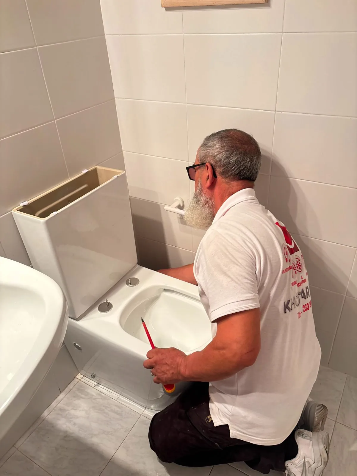 Fontanero arreglando un inodoro con la tapa de la cisterna retirada en un baño