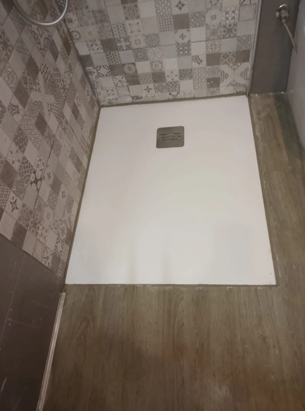 Plato de ducha blanco de resina instalado junto a pared de azulejos hidráulicos y suelo de imitación madera