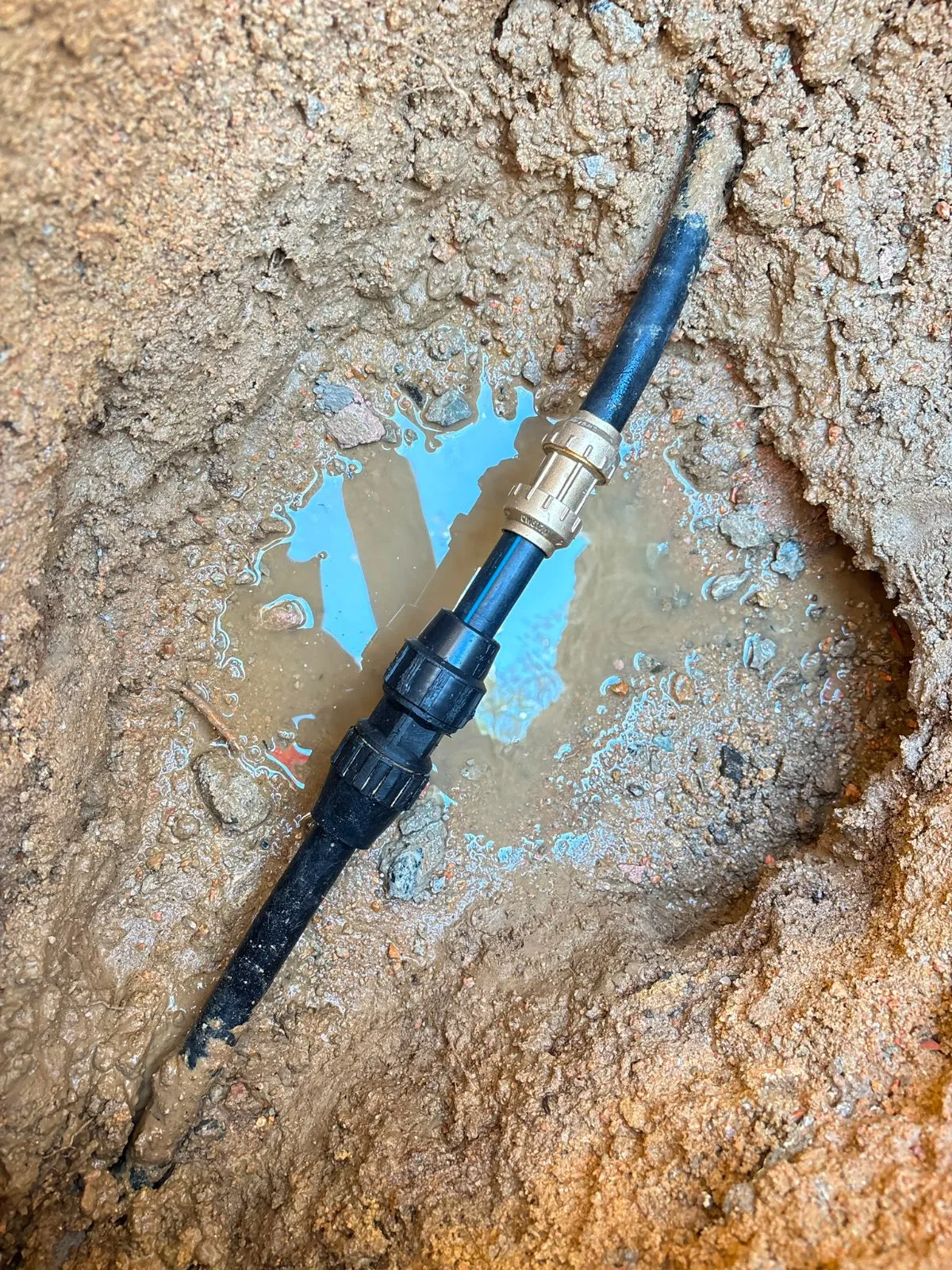 Tubería de polietileno negra con empalme reparado en una zanja de tierra con agua