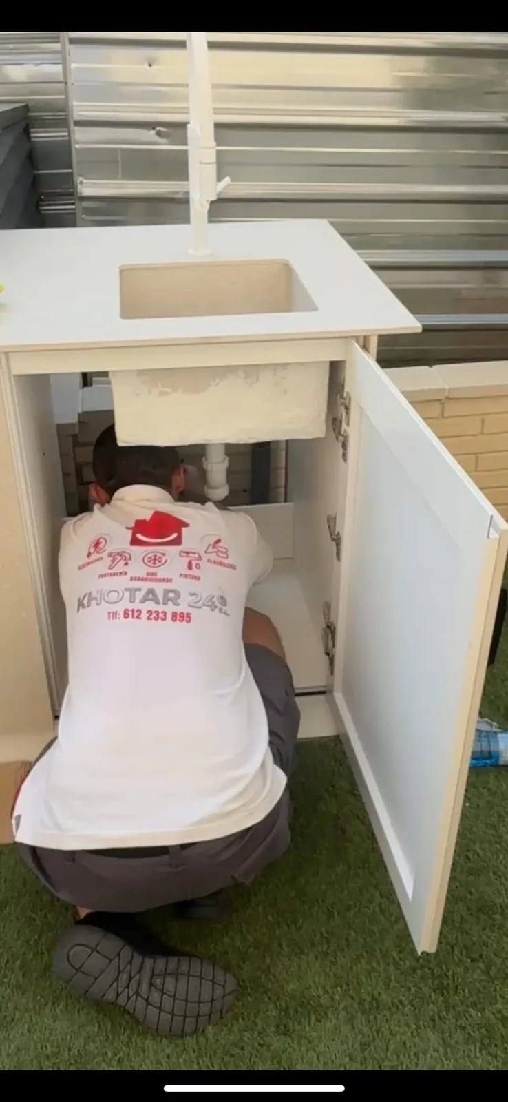 Fontanero revisando la instalación bajo un fregadero de exterior con mueble blanco